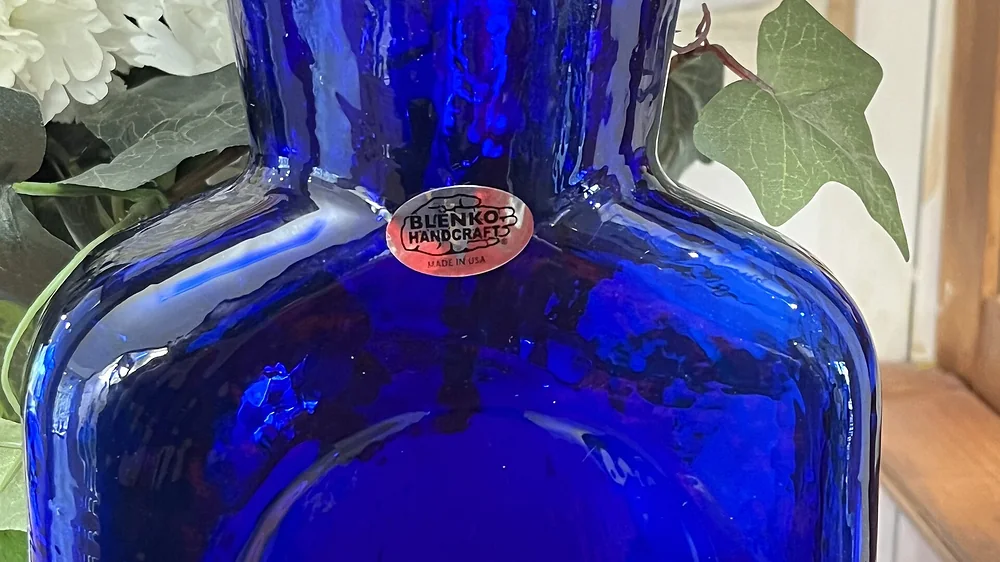 Cobalt blue hand-blown Blenko 384 water bottle with the Blenko Handcraft label on a wooden shelf