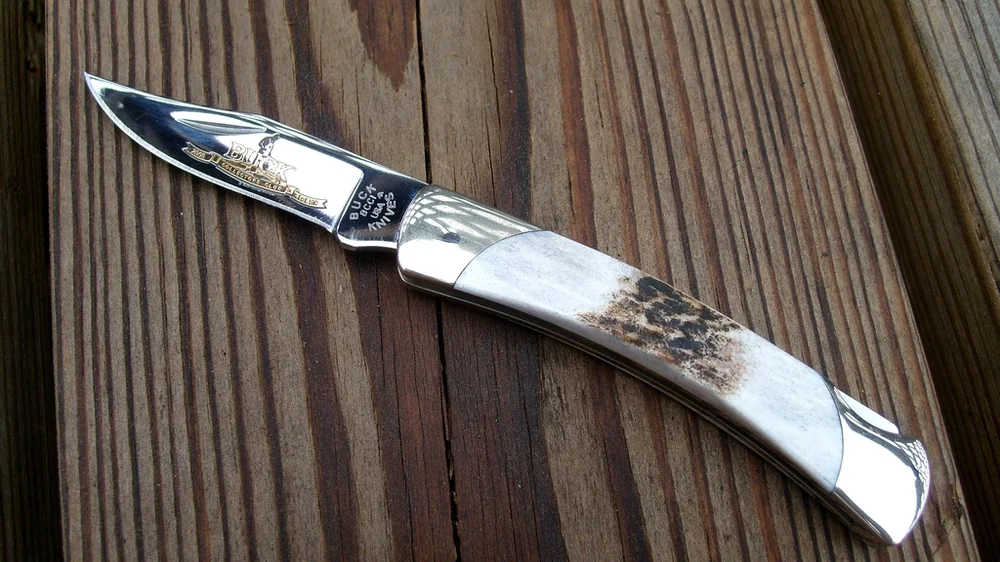 Small Buck folding knife with an open blade on a wooden deck. Representative photo, not the exact product.