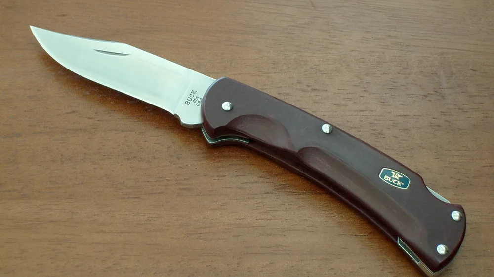 Buck 112 Ranger folding knife with a dark paperstone handle on a wooden table. Representative photo, not the exact product.