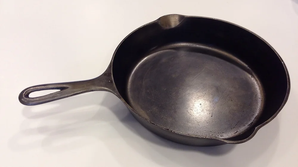 A well-used cast iron skillet on a white surface. Representative photo, not the exact product.