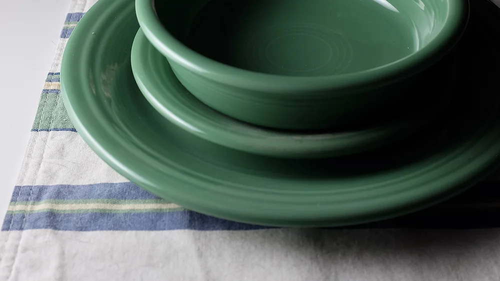 Green Fiesta dinnerware bowl stacked on a plate on a striped cloth