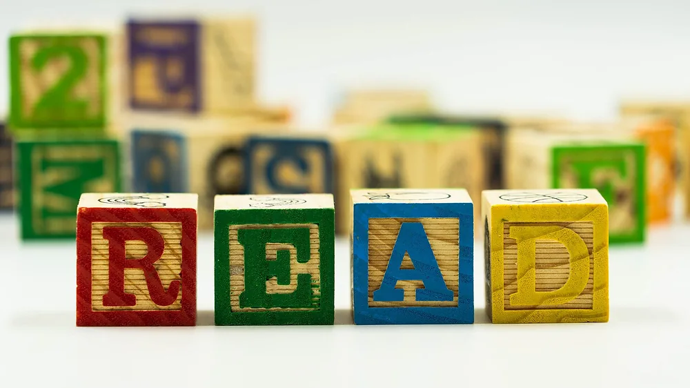 Wooden alphabet blocks spelling the word READ with more blocks behind. Representative photo, not the exact product.