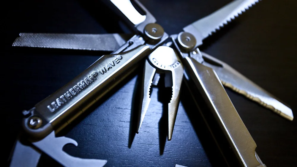 Leatherman Wave multitool with its pliers, saw, knife, scissors and other tools fanned open on a dark surface