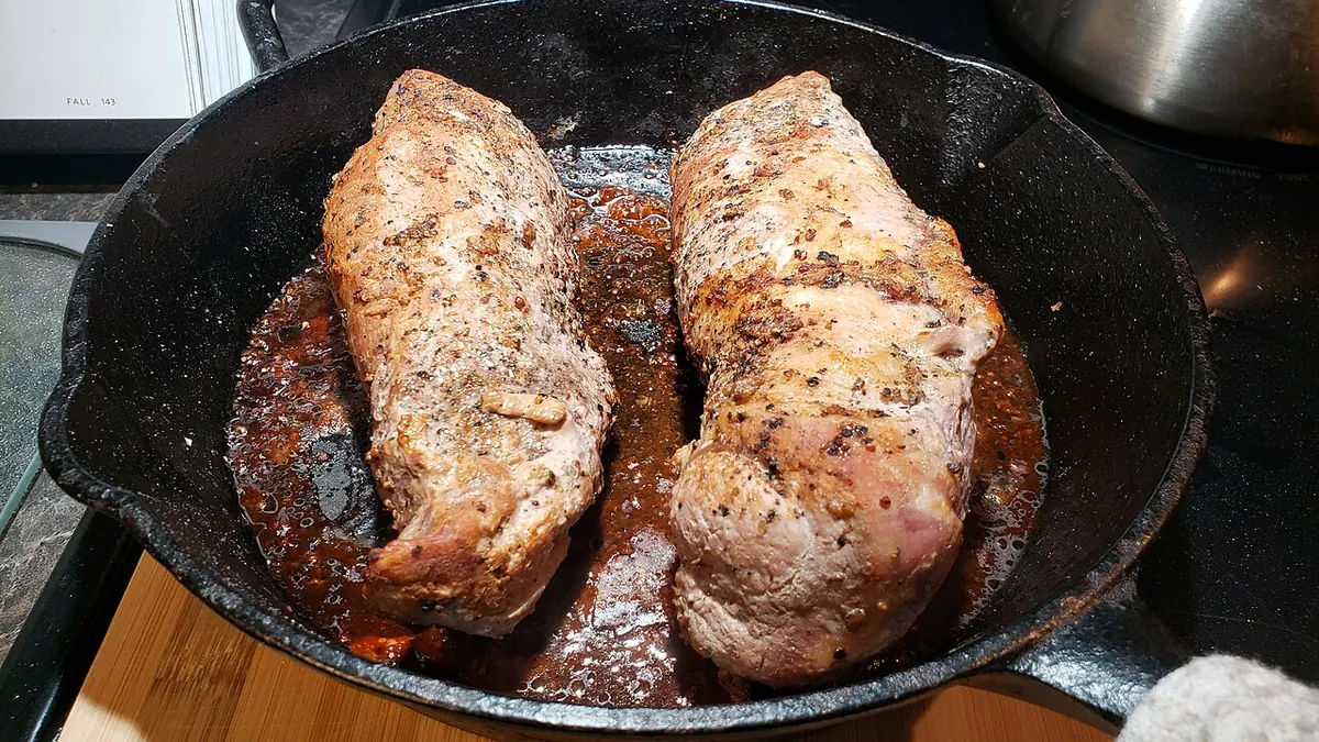 Pork tenderloin searing in a cast iron skillet on a stove