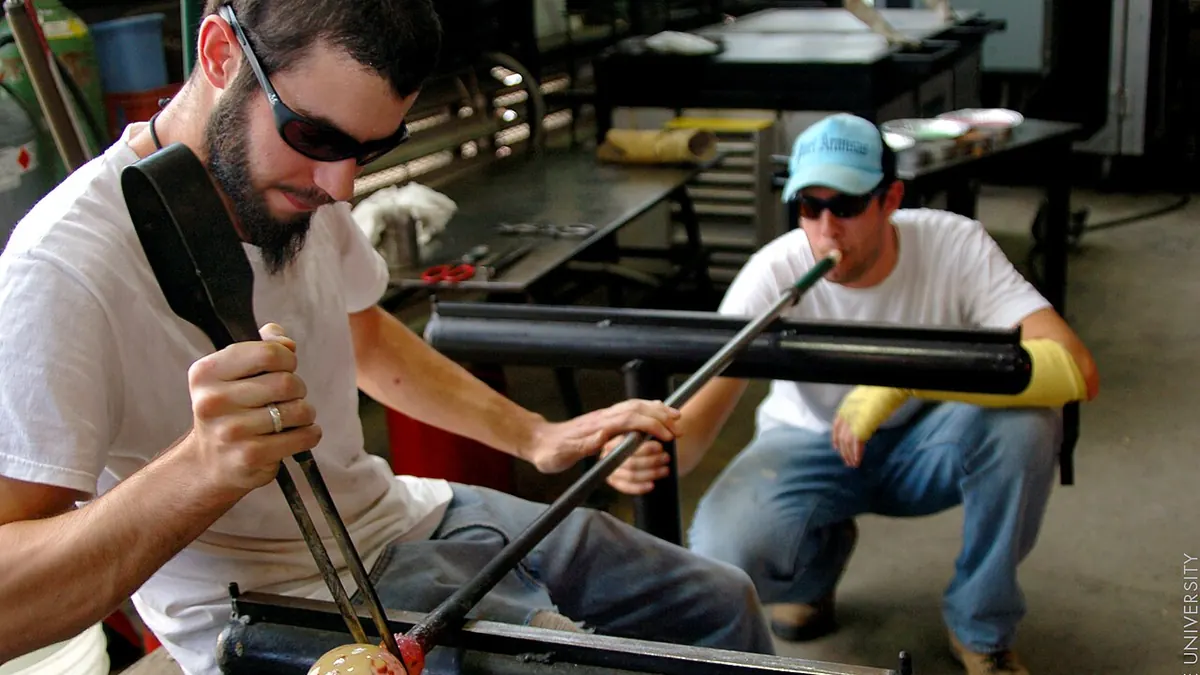 Two glassblowers shaping molten glass at a studio furnace